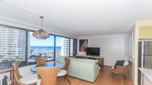 A modern living room with a large window, a dining area with wicker chairs, a sofa, and a flat-screen TV. - Perfect Waikiki Location, Right Near The Beach! (Honolulu)