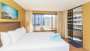 A hotel room with a large bed, a painting of a beach scene, a view of high-rise buildings, and a balcony with a railing. - Perfect Waikiki Location, Right Near The Beach! (Honolulu)
