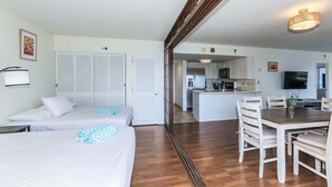 Une chambre d’hôtel avec deux lits, une table à manger avec des chaises, un coin cuisine et un téléviseur.