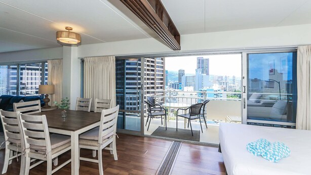 Une chambre d’hôtel avec un balcon, un coin repas avec des chaises et une table, et un lit avec un oreiller bleu.