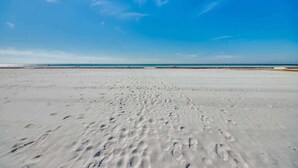 Una extensa playa de arena con huellas que se adentran en el agua bajo un cielo azul despejado.