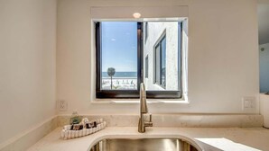 Una cocina con un lavaplatos de acero inoxidable, una ventana con vista a la playa y una encimera con un escurreplatos.