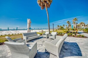 An outdoor seating area with wicker furniture, a palm tree, and a view of the beach.