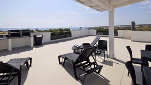 Eine Dachterrasse mit Gartenmöbeln, einer Pergola und Blick auf das Meer.