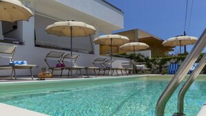 Ein Swimmingpool mit Liegestühlen und Sonnenschirmen, umgeben von einem Gebäude mit heller Fassade.