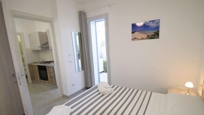 Ein Hotelzimmer mit Bett, Nachttischlampe, einem Strandbild und Blick ins Freie.
