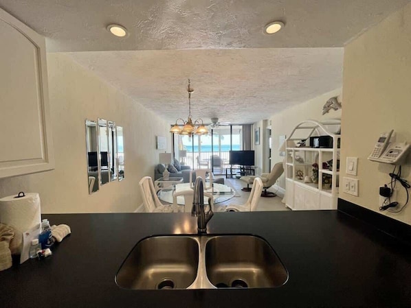 A modern kitchen with a double sink, a dining area with a round table and chairs, and a view of the ocean through large windows.