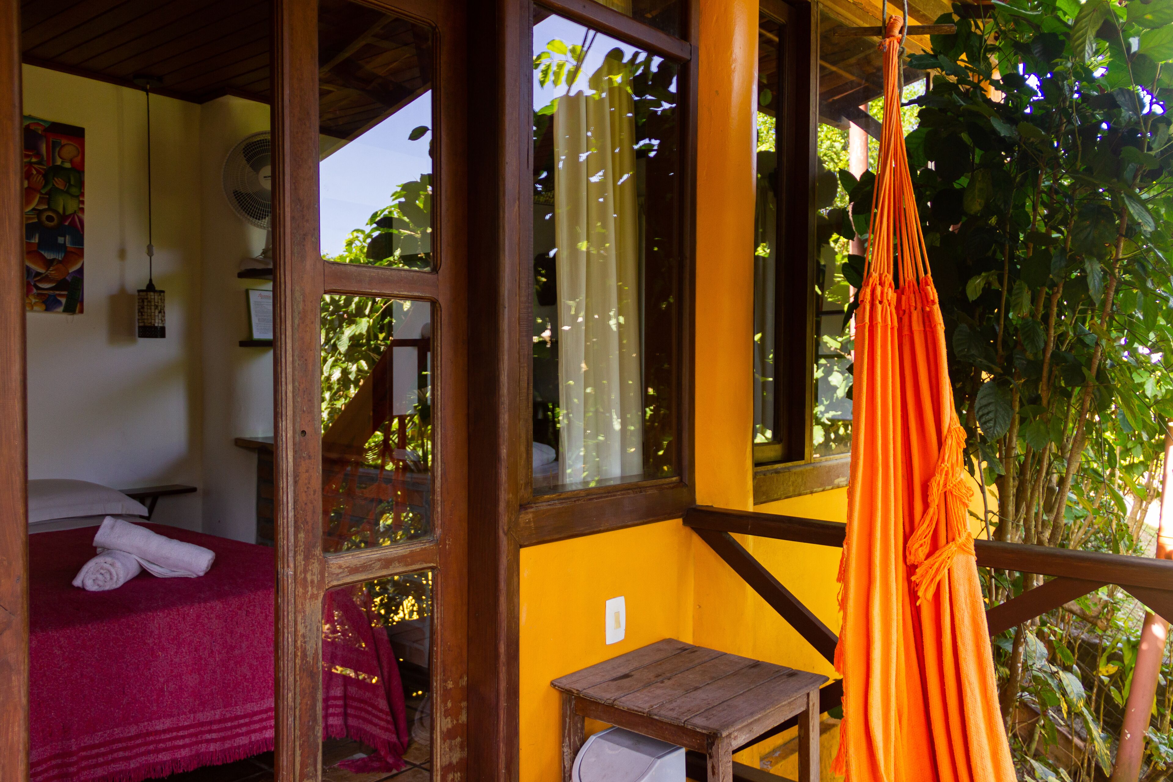 Una habitación con una cama, una mesita pequeña y una hamaca naranja colgada.