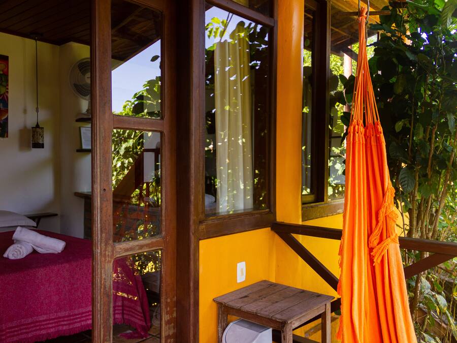 Una habitación con una cama, una mesita pequeña y una hamaca naranja colgada.