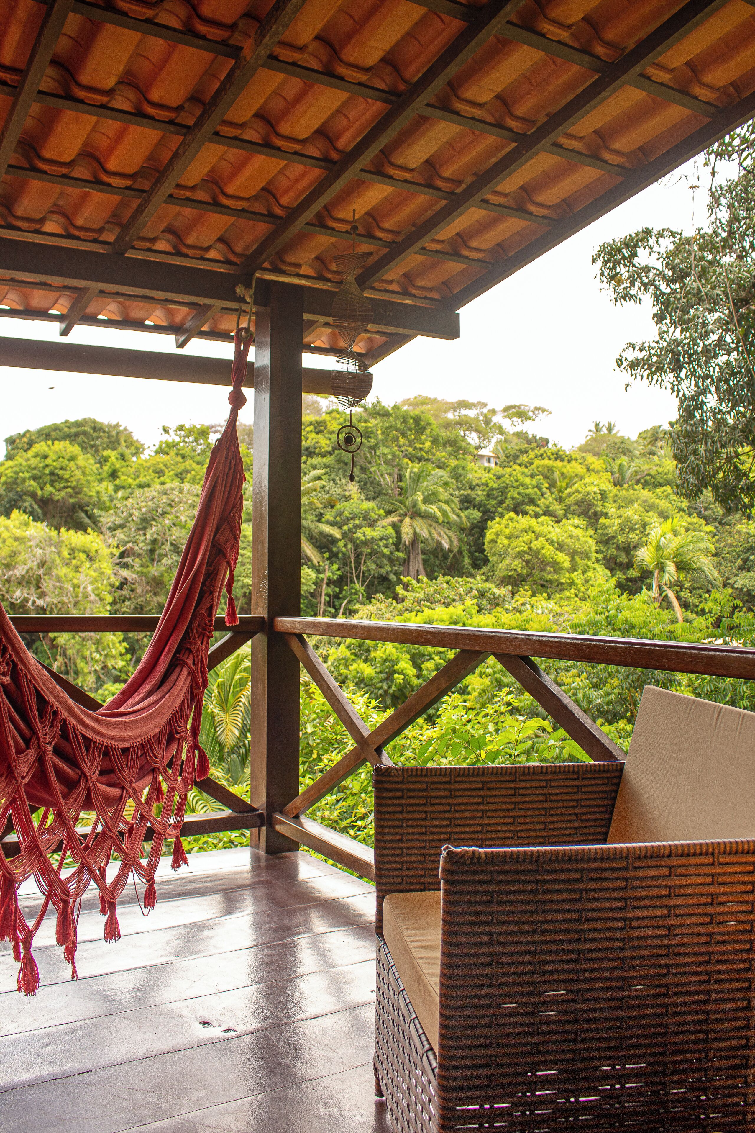A wooden deck with a hammock and wicker furniture overlooking a lush green landscape.