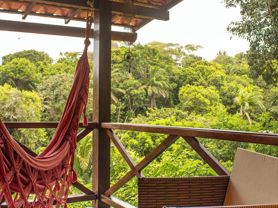 A wooden deck with a hammock and wicker furniture overlooking a lush green landscape.