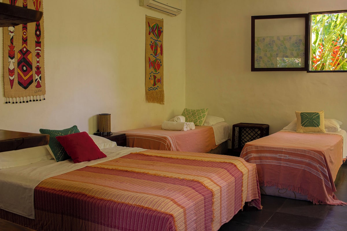 Une chambre d’hôtel avec deux lits simples, une grande fenêtre donnant sur un paysage verdoyant et une décoration murale représentant des motifs de poissons.