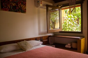 Un dormitorio con cama, una ventana con vistas a zonas verdes, una mesita de noche y un aire acondicionado instalado en la pared.