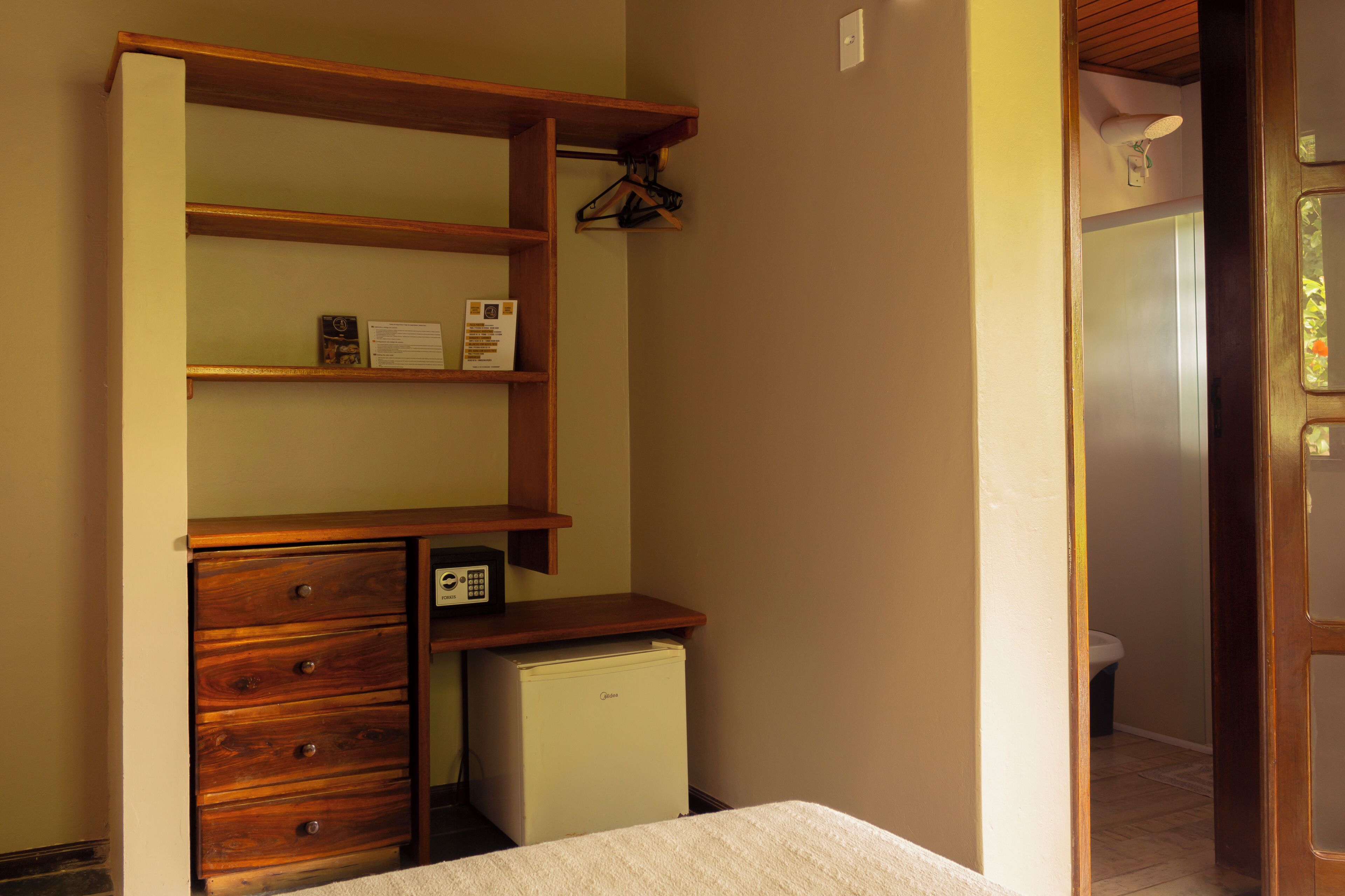 A compact room with a wooden dresser, a small refrigerator, and a bed.