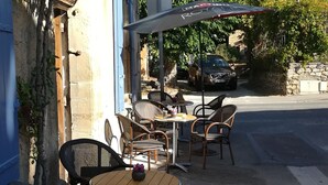 An outdoor café with wicker chairs and tables, a stone wall, and a parked car in the background. - PRETTY PROVENCAL VILLA IN THE HEART OF THE LUBÉRON PARK 7 MIN FROM GORDES (Saint-Saturnin-lès-Apt)
