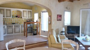 A spacious living area with a sofa, a dining table, and a TV. There is a kitchen with cabinets and a window. - PRETTY PROVENCAL VILLA IN THE HEART OF THE LUBÉRON PARK 7 MIN FROM GORDES (Saint-Saturnin-lès-Apt)