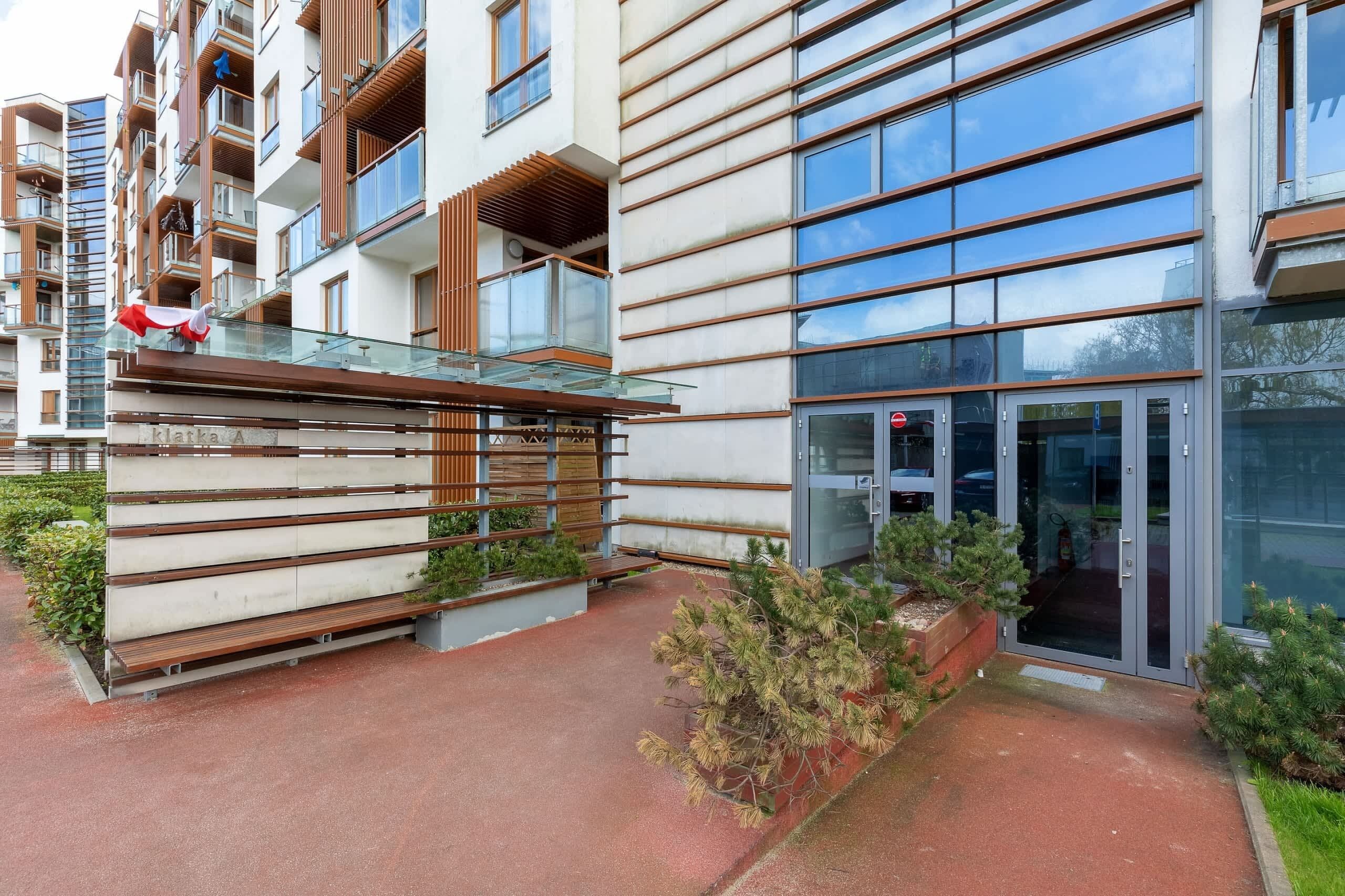 Een modern gebouw met een glazen entree, houten balkons en een pad van rode bakstenen.