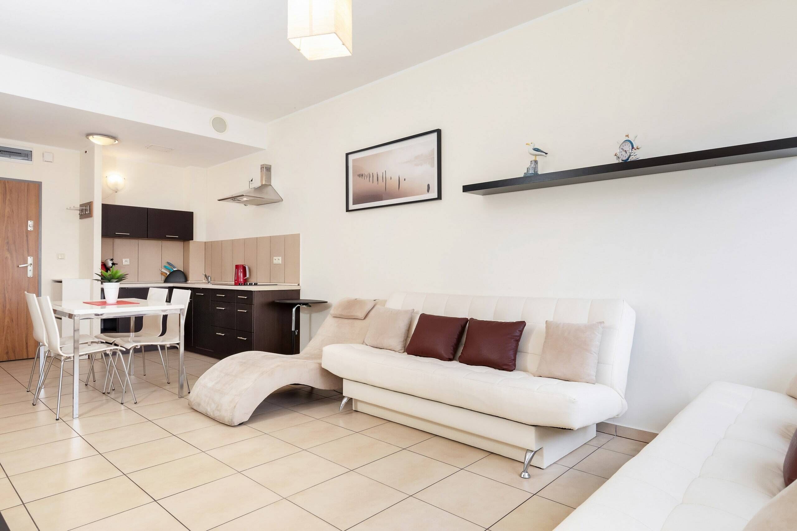 A bright living room with a comfortable white sofa, a coffee table, and a mounted flat-screen TV, creating a relaxing area to unwind.