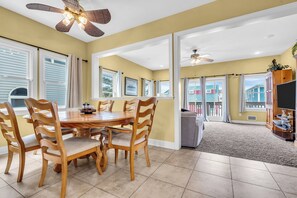 A dining area with a wooden table and chairs, a ceiling fan, and large windows with curtains.