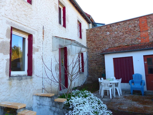 A white building with red shutters, a stone wall, and a small garden with white flowers.