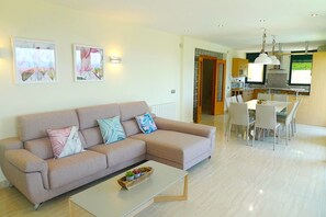 A modern living room with a beige sofa, a coffee table, and a dining area with a table and chairs. There are two framed artworks on the wall. - Luxury villa Vista del Mar with stunning sea views, pool, walk to the beach (Lloret de Mar)