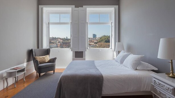 A bedroom with a bed, a chair, a nightstand, and a lamp. - GuestReady - Innvict Admiral (Porto)