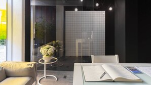 A modern interior with a glass partition, a white tiled wall, a small table with a vase of flowers, and a seating area with a sofa and chairs. - GuestReady - Innvict Admiral (Porto)
