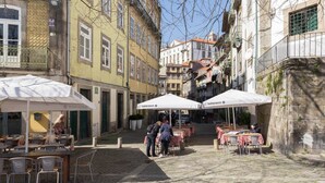 A cobblestone street with outdoor seating under white umbrellas, a café named 'Super Bock', and buildings with balconies and windows. - GuestReady - Innvict Admiral (Porto)