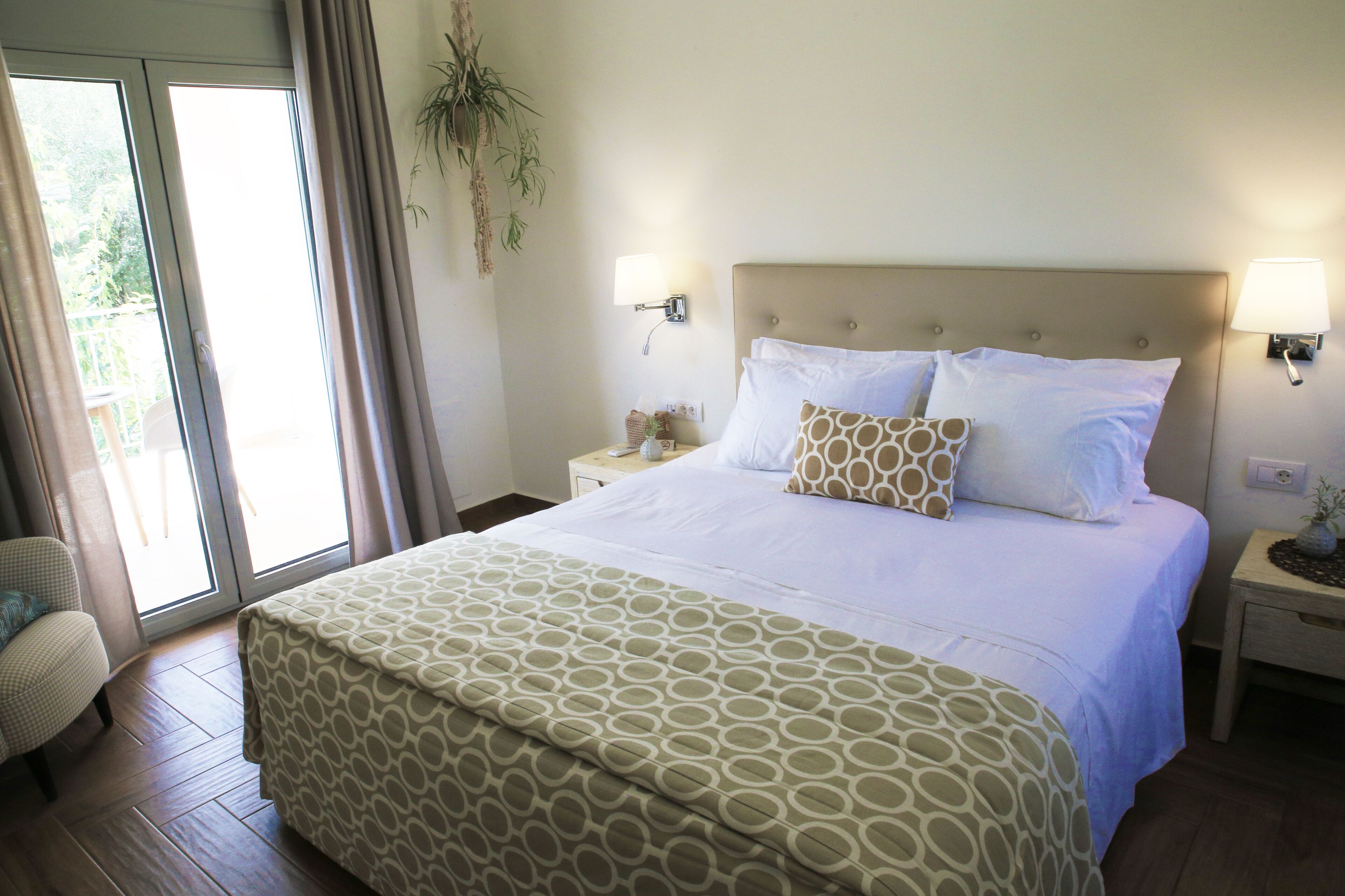 A hotel room with a large bed, two bedside tables, a chair, and a sliding glass door leading to an outdoor area.