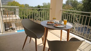 A balcony with a table set for breakfast, including plates, a cup, and a glass of orange juice. - Amarianos Villas (Kefalonia)