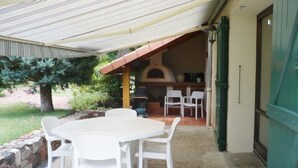 Un patio al aire libre con una mesa, sillas, un horno de ladrillo y una puerta verde.