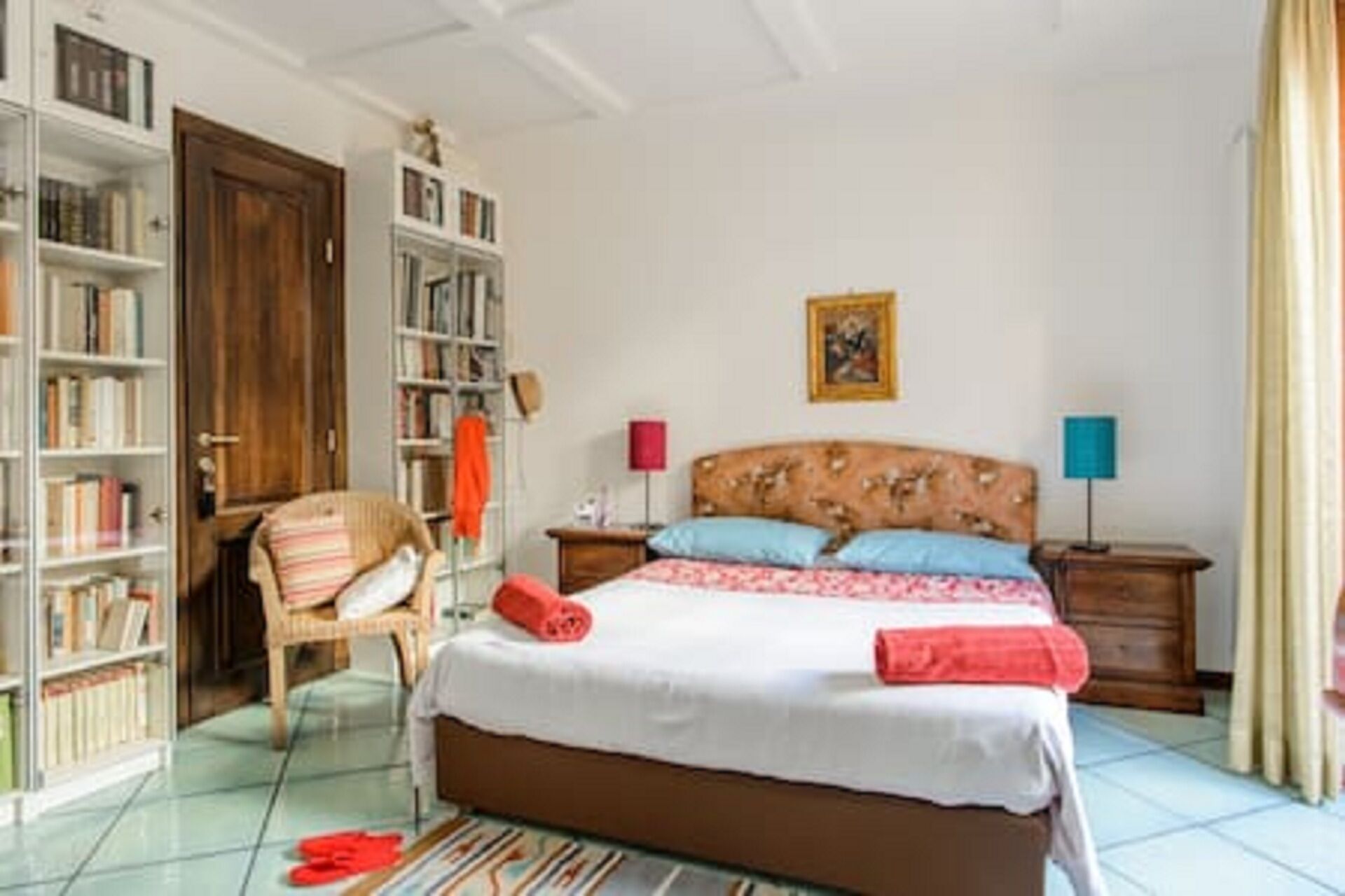Ein Schlafzimmer mit einem Bett, zwei Nachttischen, einem Sessel, einem Bücherregal und einer Tür.