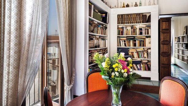A dining area with a wooden table, chairs, a vase with flowers, and a bookshelf filled with books. - Naples Center Apartment (Napoli)