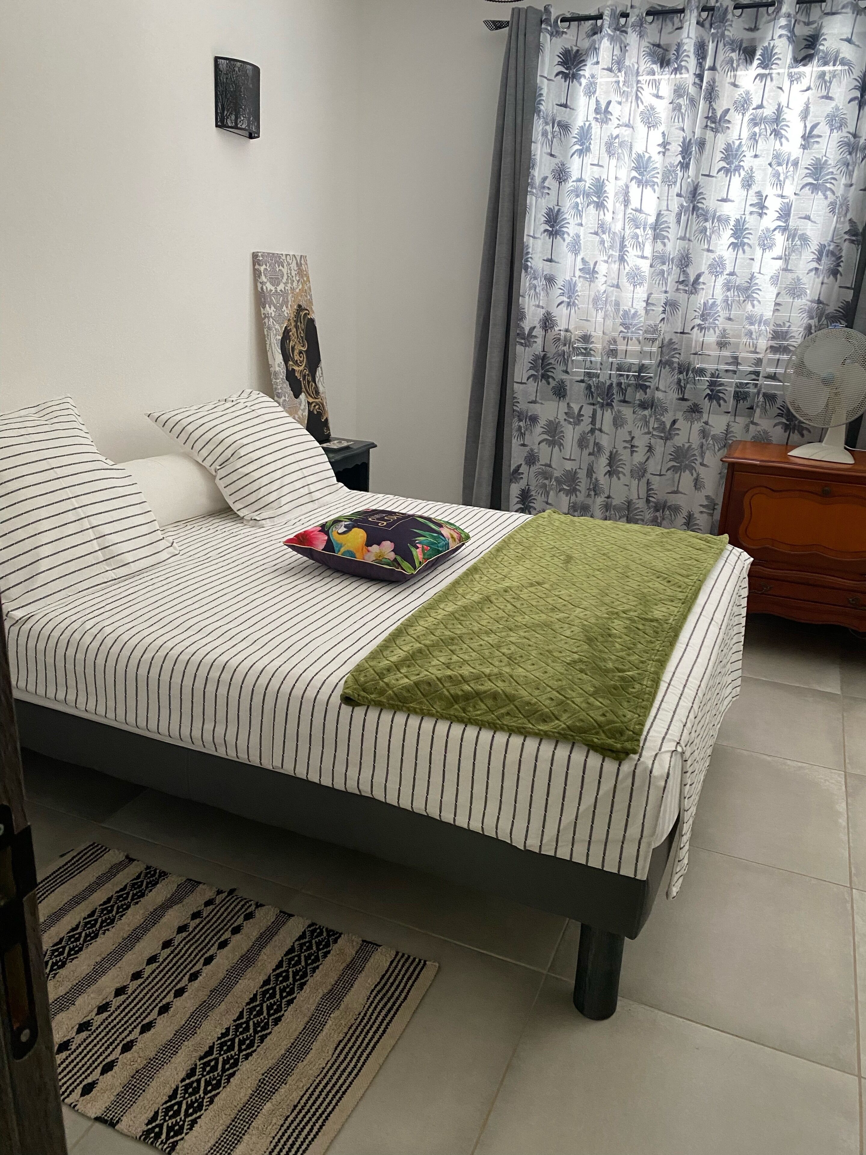 Una cama bien hecha con ropa de cama a rayas, un plaid verde y una almohada colorida.