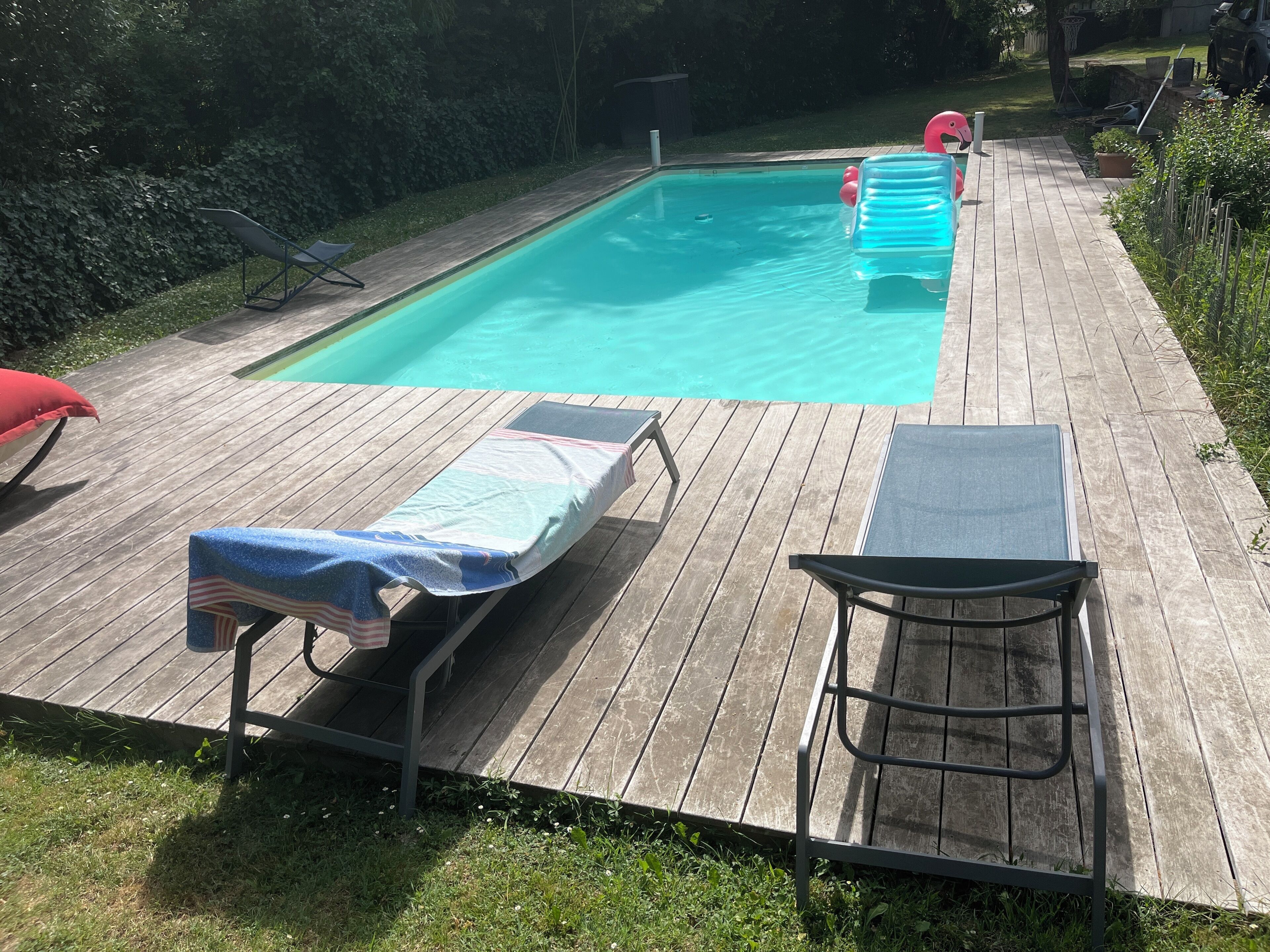 A wooden deck with a swimming pool, lounge chairs, and a sunbed.