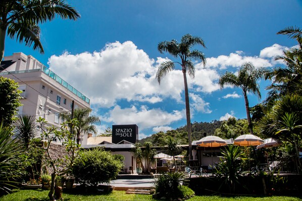 A hotel named "Spazio del Sole" with a clear blue sky, palm trees, and a well-maintained garden. - Spazio del Sole Jurere (Florianópolis)