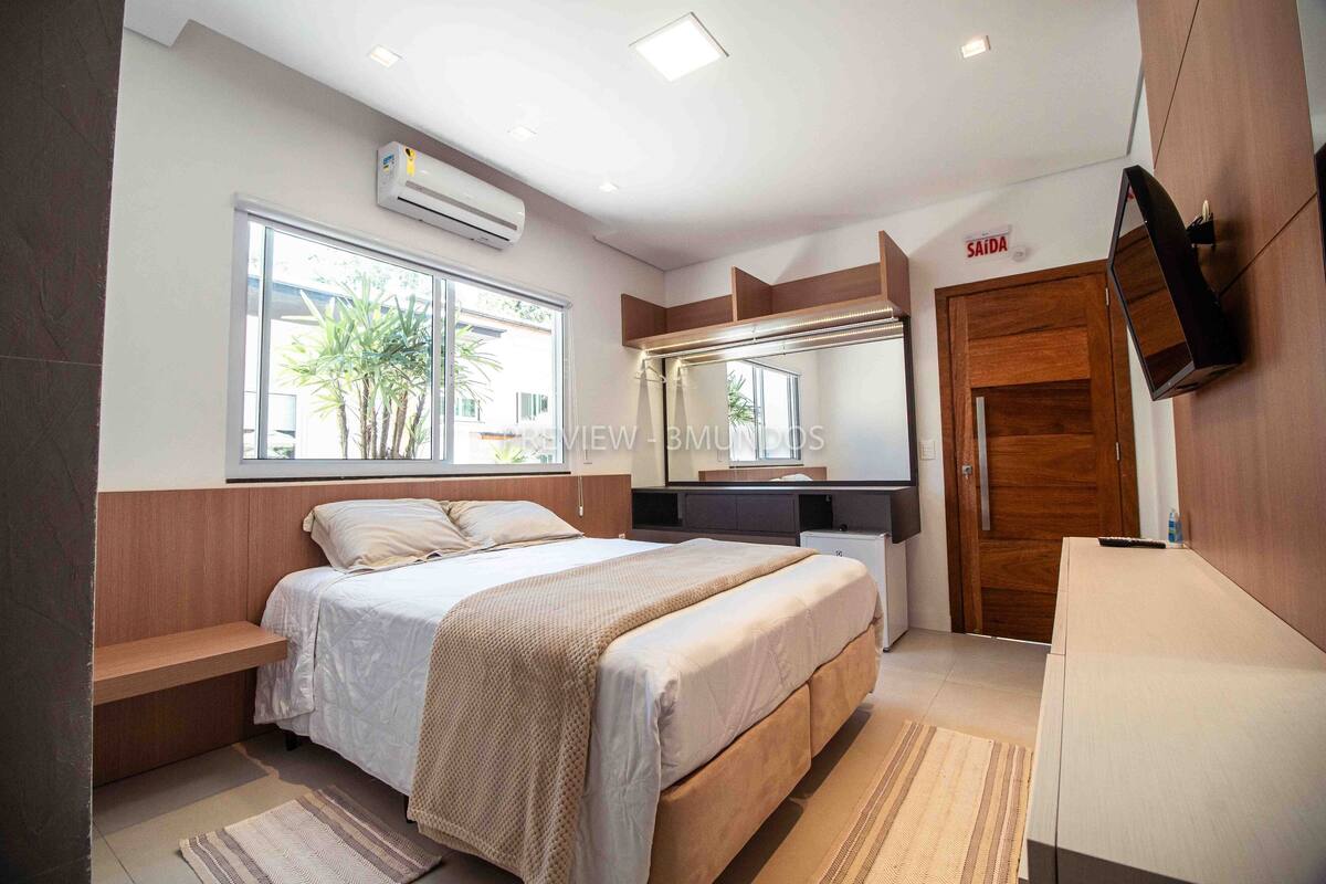 Ein modernes Schlafzimmer mit Bett, Einbauschränken, Fernseher und großem Fenster.