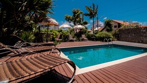 A swimming pool with lounge chairs and umbrellas, surrounded by greenery and buildings. - Spazio del Sole Jurere (Florianópolis)