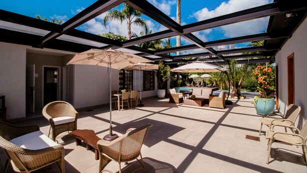 A covered outdoor patio with wicker furniture, umbrellas, and a pool area. - Spazio del Sole Jurere (Florianópolis)