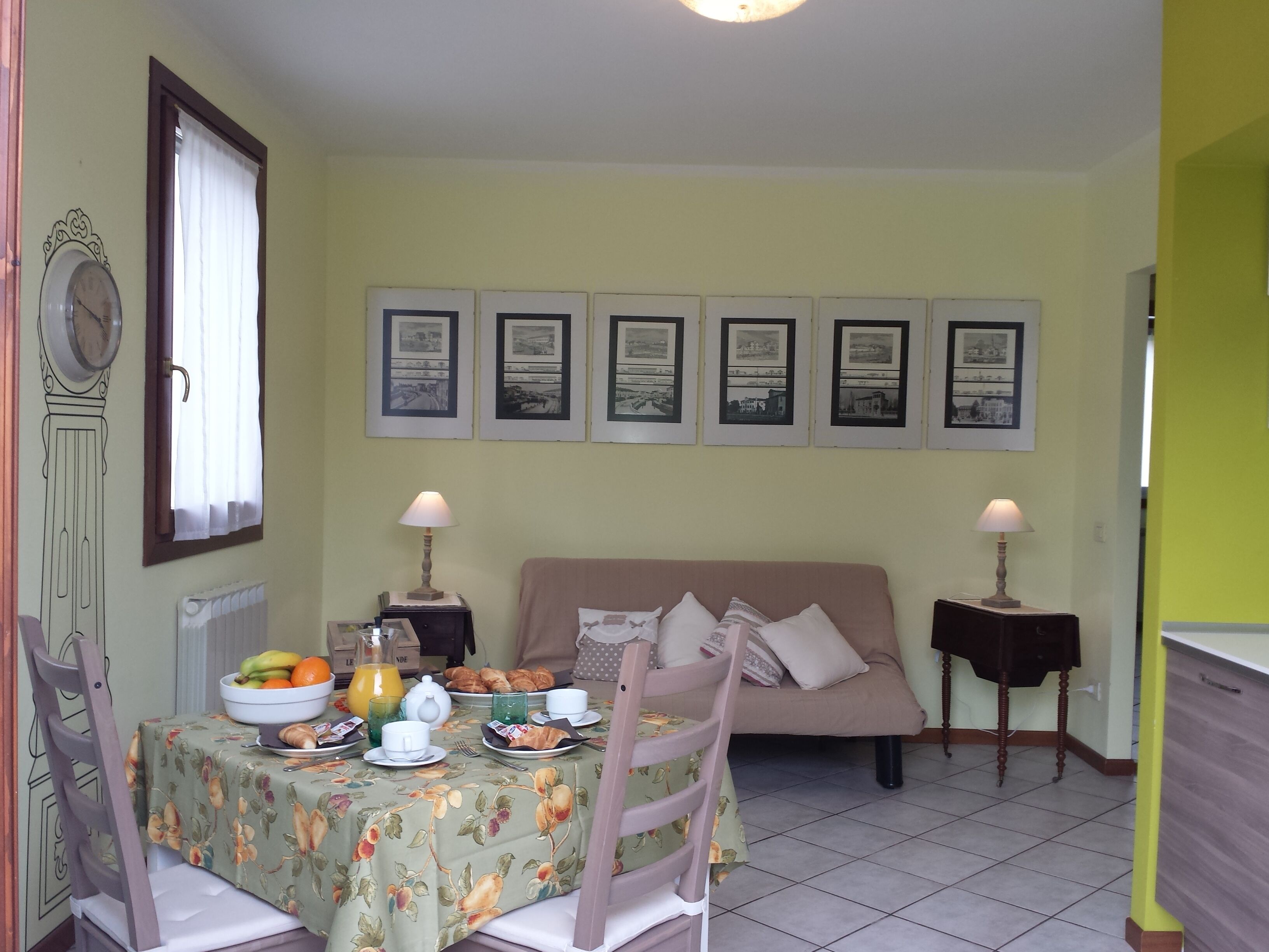 A dining area with a table set for breakfast, a sofa, and framed pictures on the wall.