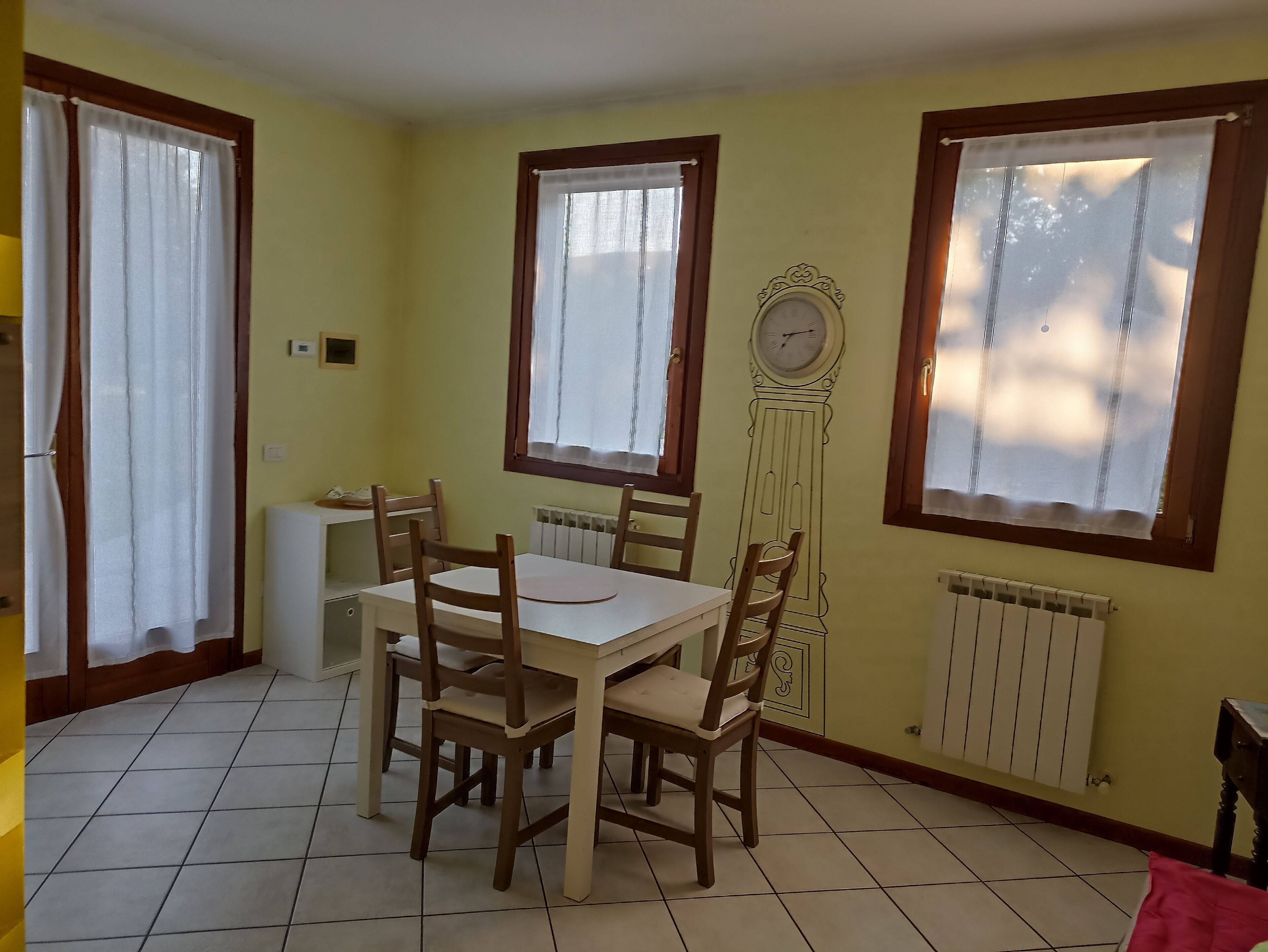 A dining area with a table and chairs, a clock on the wall, and windows with curtains.