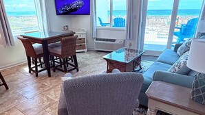 Een woonkamer met een televisie, rieten meubels, een glazen salontafel en een bank.