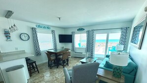 Een woonkamer met een eethoek, een aan de muur bevestigde televisie en uitzicht op zee.