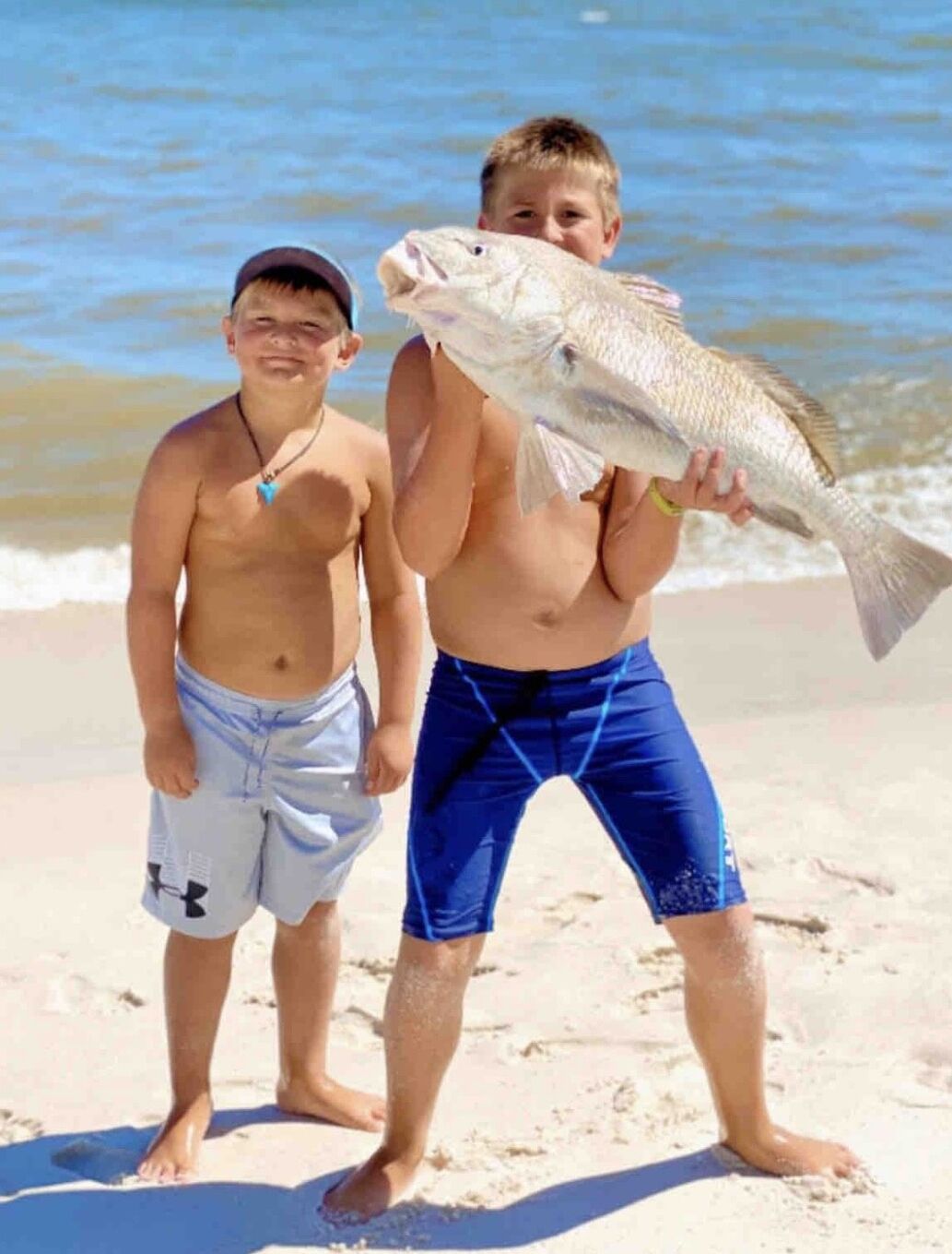 Deux personnes se trouvent sur une plage et tiennent un poisson.