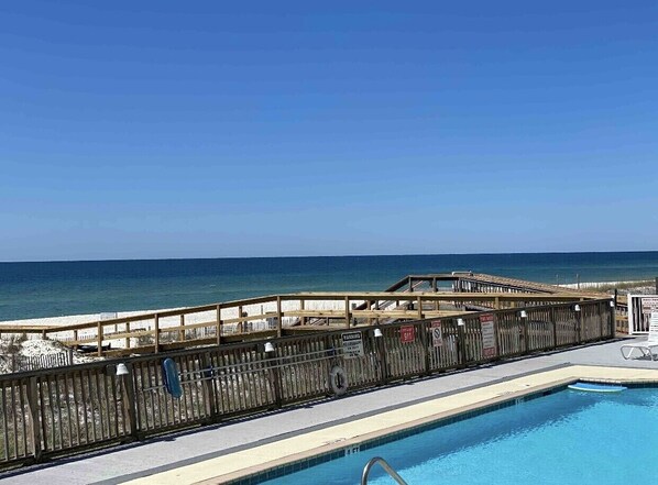 A pool area with a wooden deck and a view of the beach.