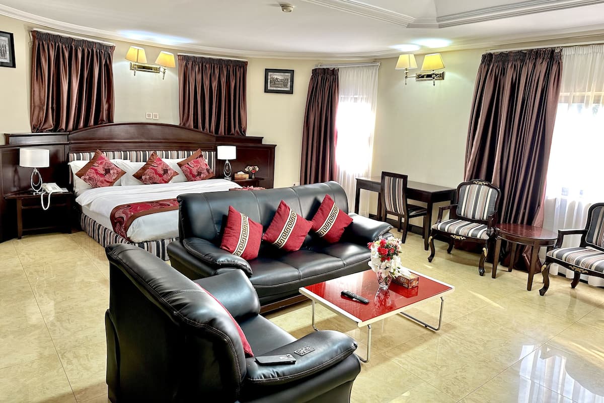 A hotel room with a large bed, a leather sofa, a dining table, and two chairs.