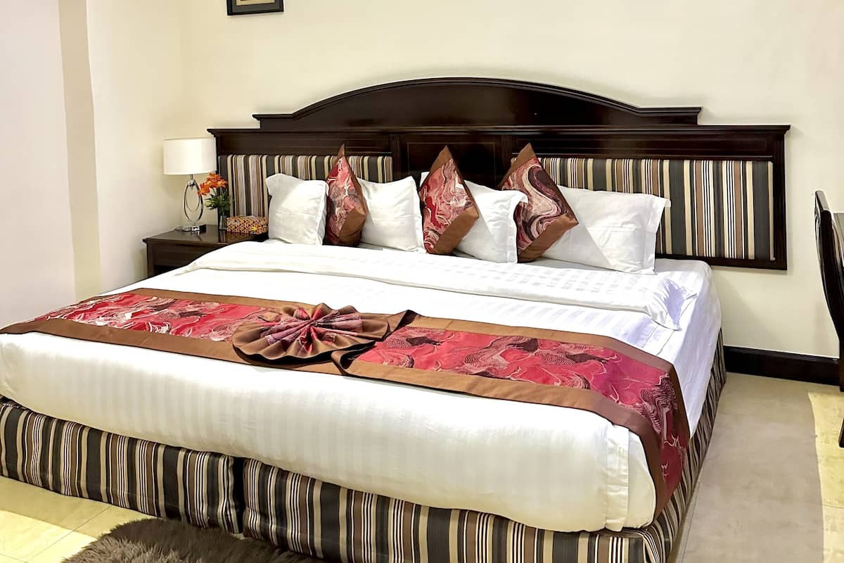 A neatly made bed with a striped bed runner, a fluffy rug, and a framed picture on the wall.