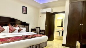 A hotel room with a large bed, a wooden headboard, a bedside table, a chair, a small desk, a mirror, and a wardrobe. - Sonia Hotel (Accra)