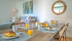 A breakfast setup with croissants, orange juice, and coffee on a wooden table in a modern room with a sofa, pillows, and a painting.