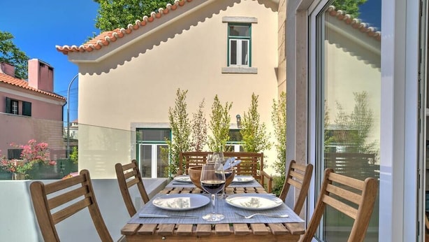 A dining table set for four with wooden chairs, a glass of red wine, and a bowl on the table.